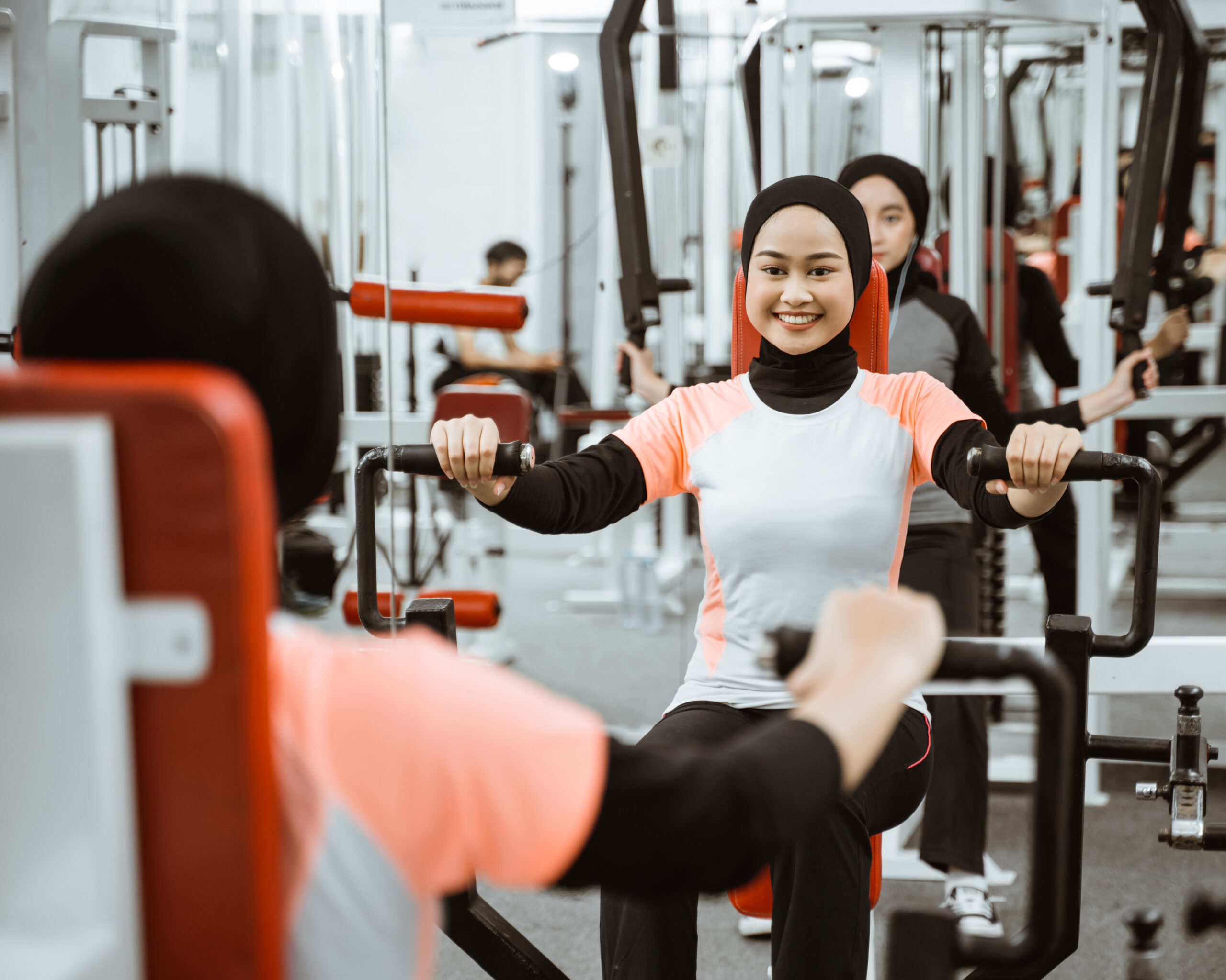 beautiful muslim asian woman using chest press machine during fitness at the gym with friend